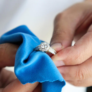 Diamond ring held on a blue cloth by hands 